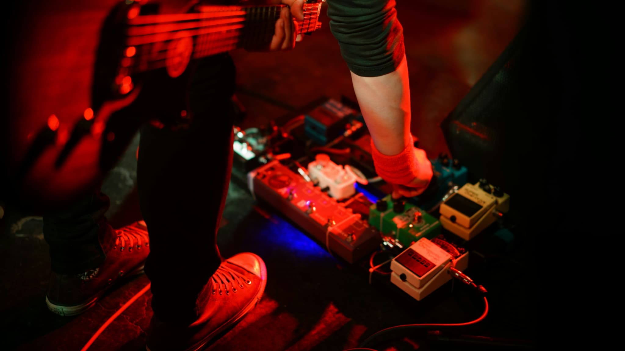 A guitarist adjusting effects pedals on stage.
