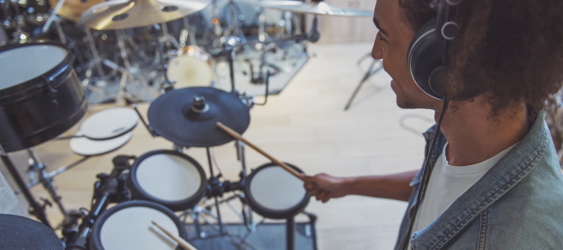 A person playing an electronic drum kit in a studio setting, wearing headphones and holding drumsticks.