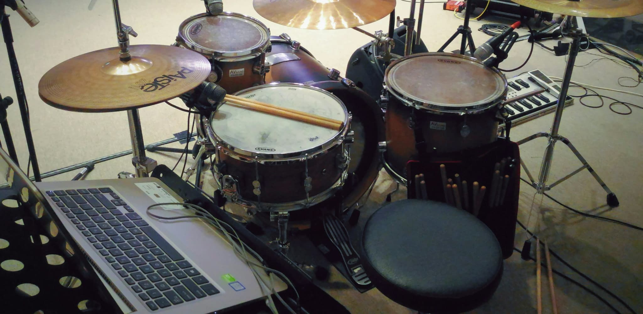 A drum kit setup with a laptop and microphones in a performance setting.
