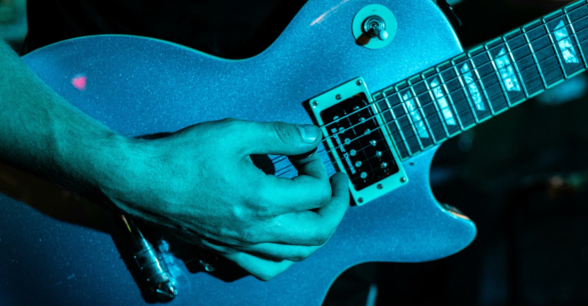 Close-up of a hand playing a blue electric guitar.