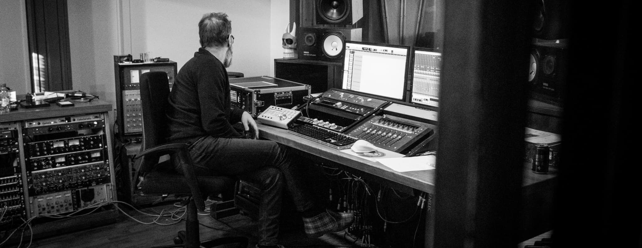 A music producer working in a professional recording studio, surrounded by audio equipment and monitors.