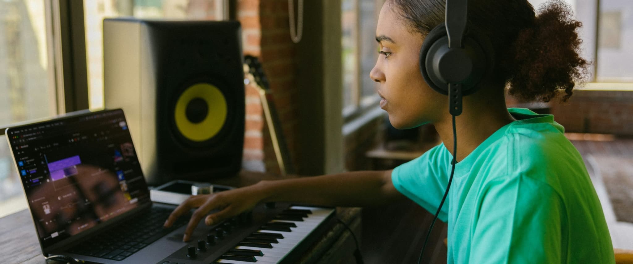 Young person using music production software with keyboard and studio monitor in a stylish workspace.