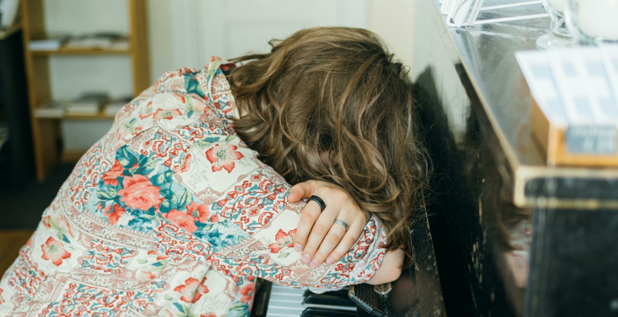 Person resting on a piano, wearing a colorful patterned shirt.